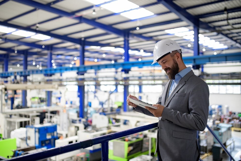 IT professional using a tablet to manage technology systems in a modern manufacturing facility.