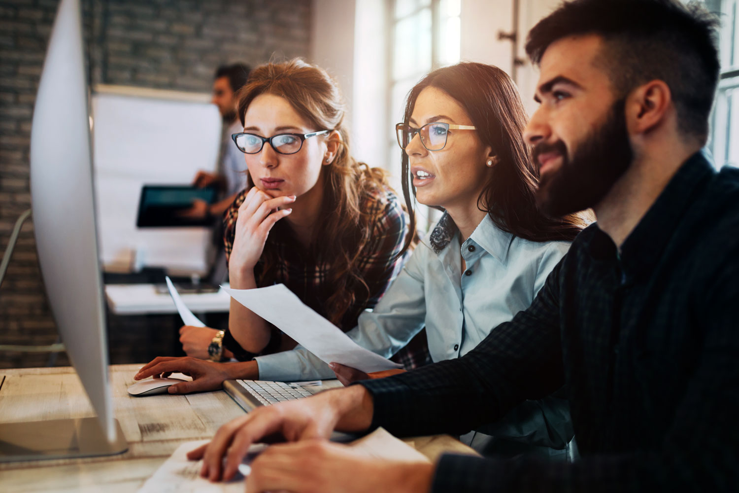 Three young professionals collaborate together and look at a computer monitor. 